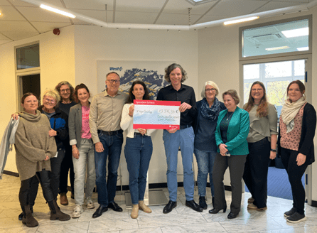 West employees posing indoors with a donation check during a community support event.