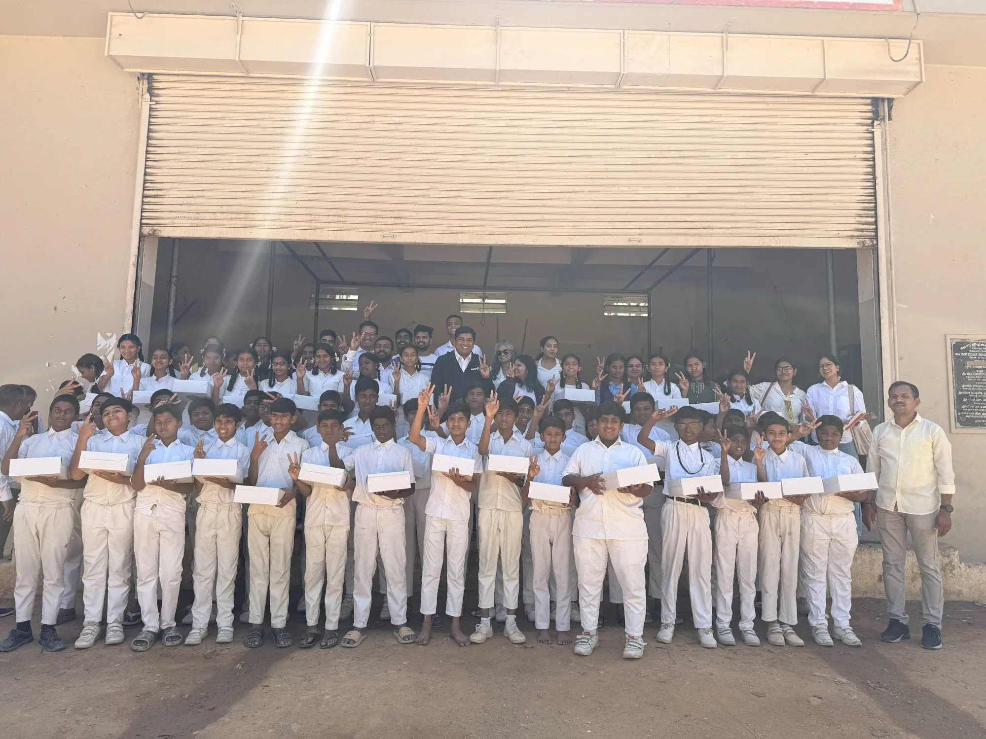 Group photo of students and volunteers holding donated laptops during the 2026 Bangalore laptop donation drive.