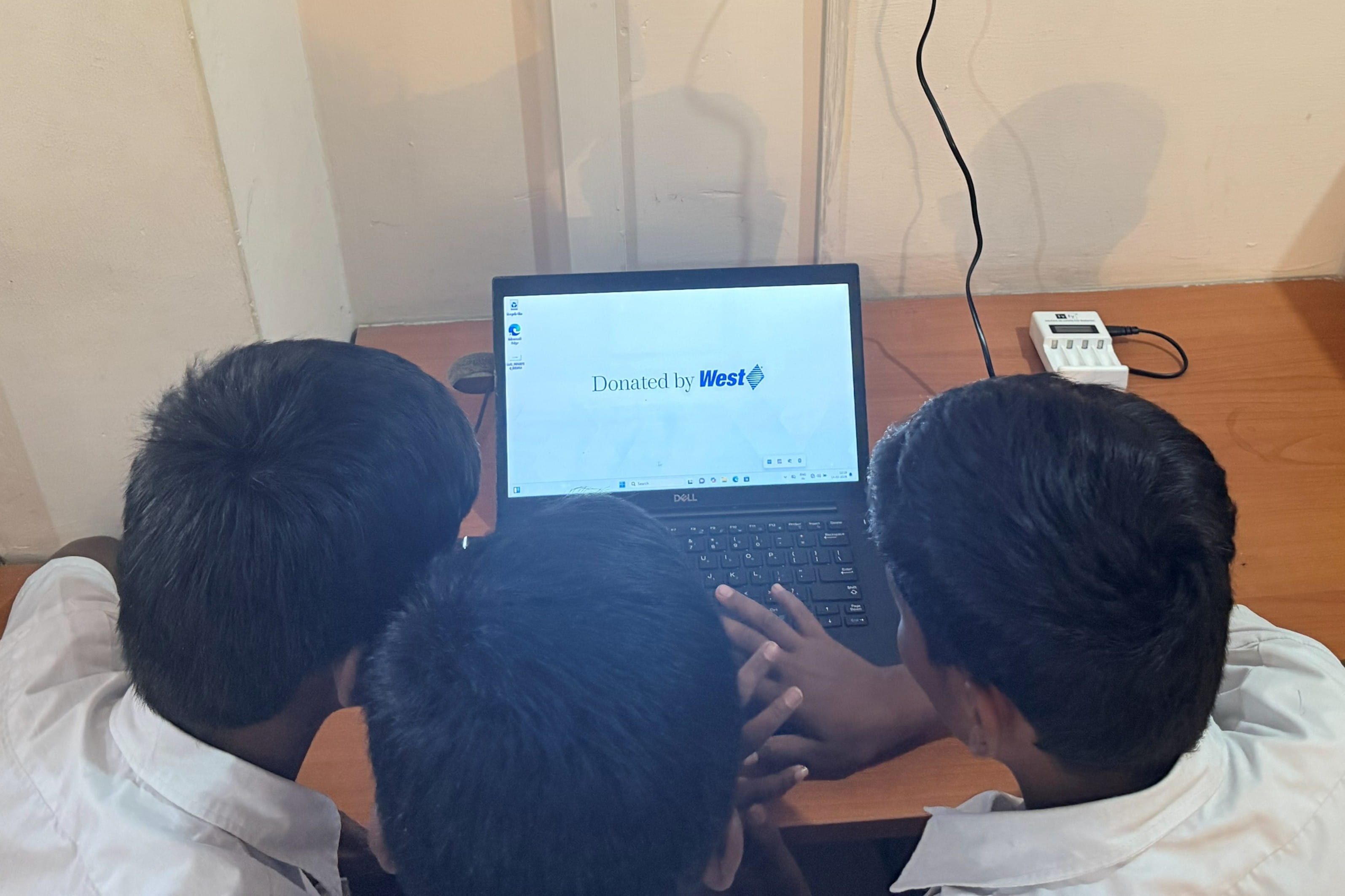 Students gathered around a donated laptop displaying “Donated by West” on the screen.