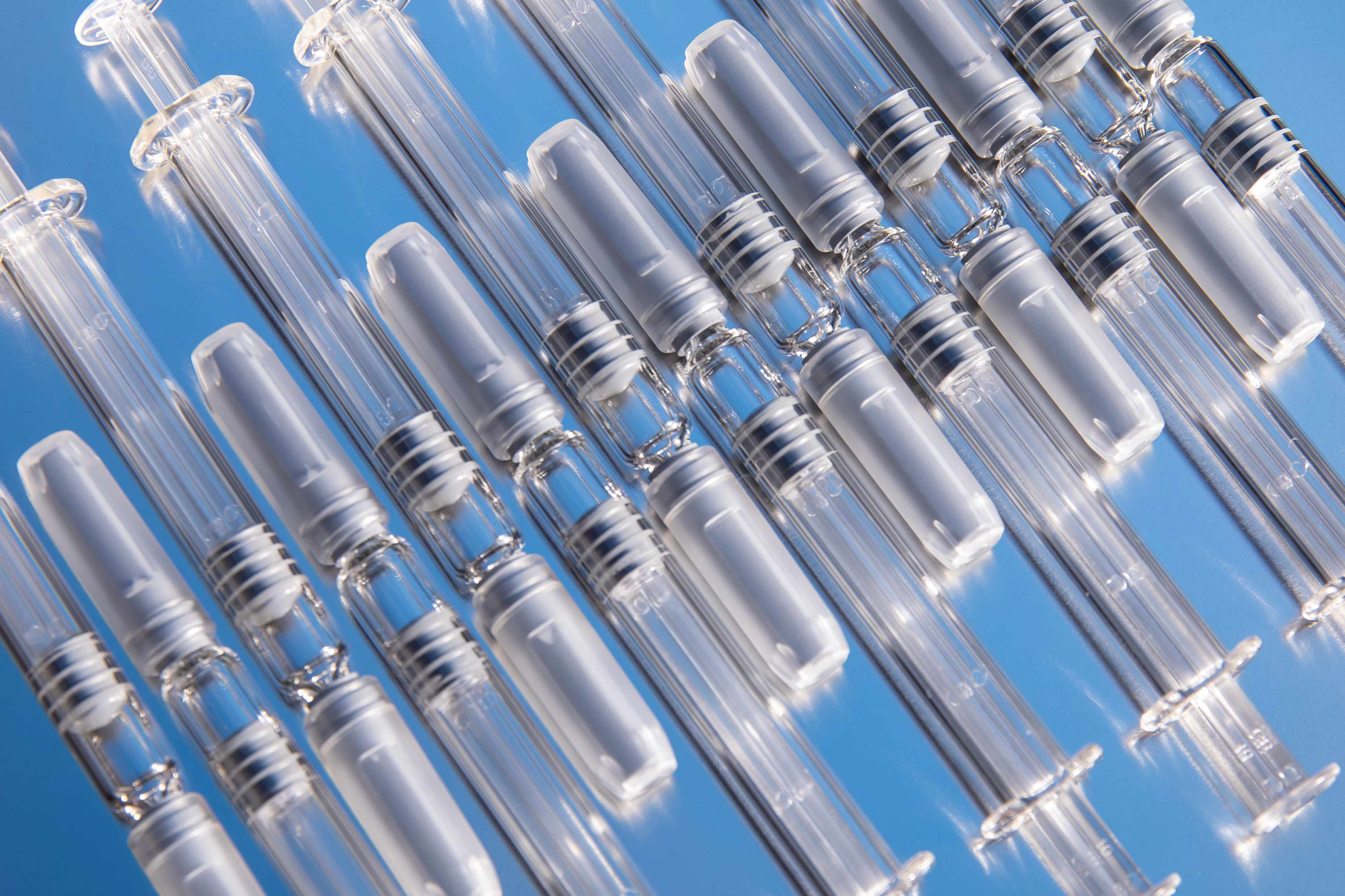 Prefillable glass syringe barrels and plungers arranged on a blue surface, illustrating a prefillable syringe system.