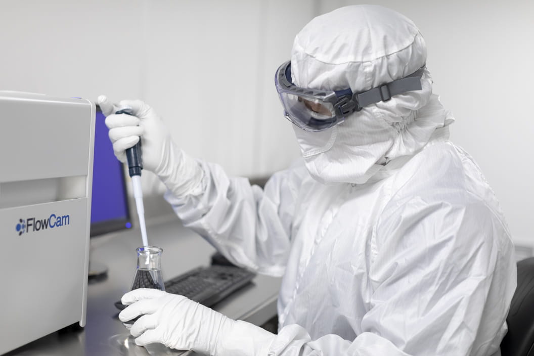 West Pharmaceutical scientist in cleanroom attire using a pipette at a laboratory workstation.