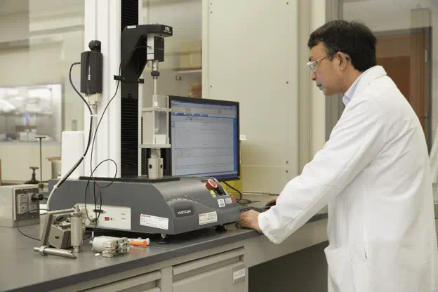 Laboratory technician operating a materials testing machine for combination product verification and performance testing.